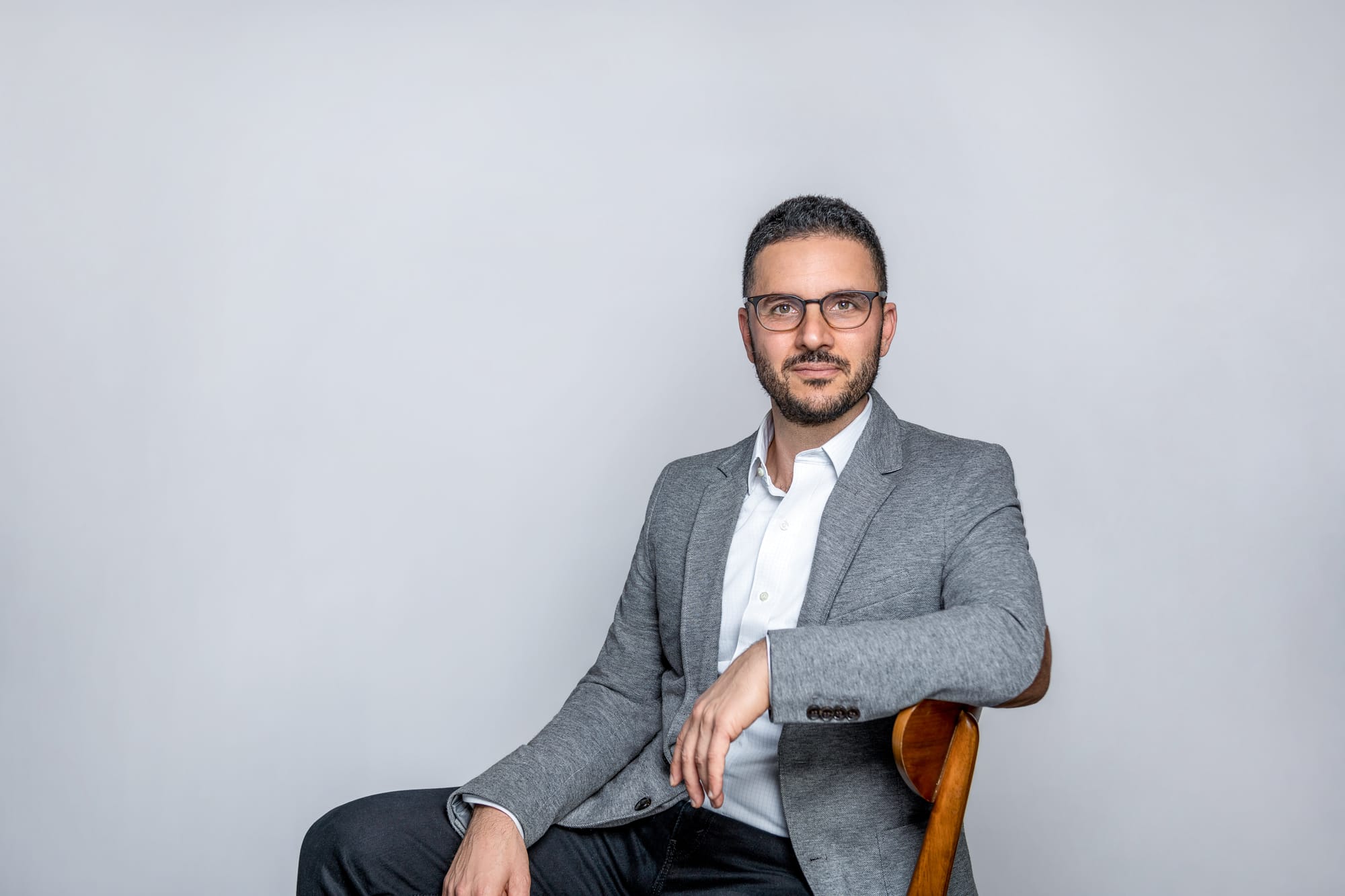 a picture of pinecone ceo edo liberty sitting on a chair wearing a gray jacket, white shirt, and dark pants